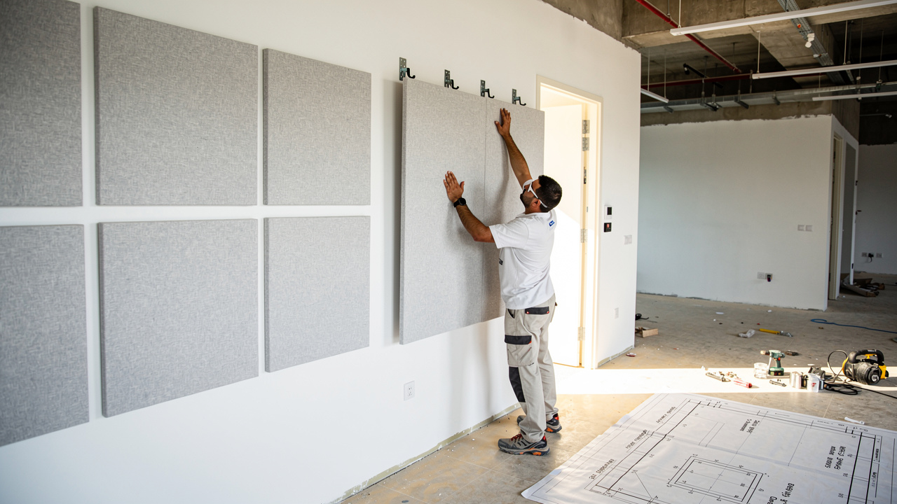 Tradesperson installing fiberglass acoustic panel on UAE office wall