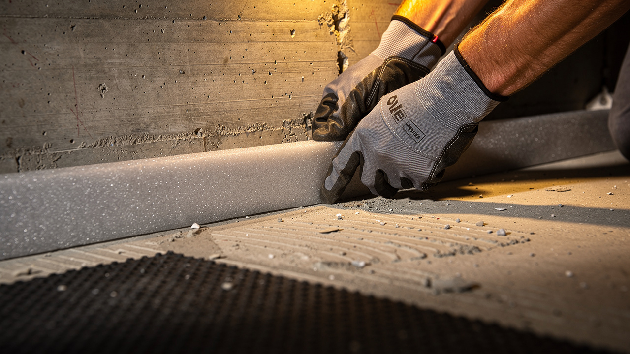 Worker installing perimeter isolation strip along apartment wall base
